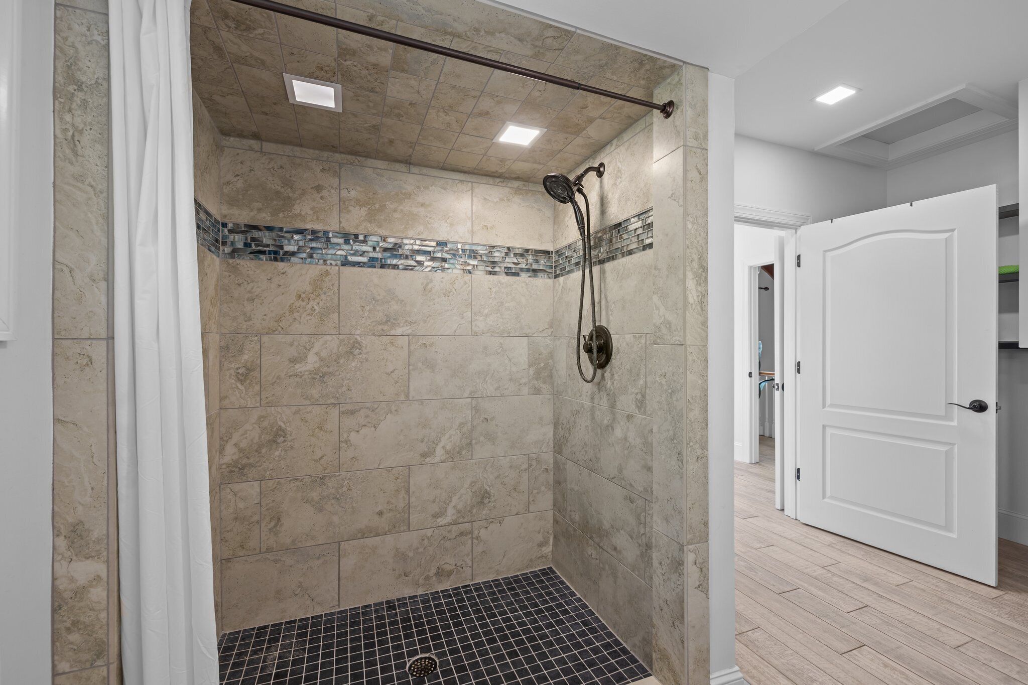 A walk-in shower with beige tiles, a showerhead, and a tiled floor.