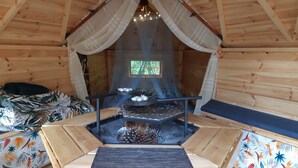 L’intérieur chaleureux d’un chalet, avec un plancher en bois, un foyer central et une fenêtre donnant sur un paysage verdoyant.