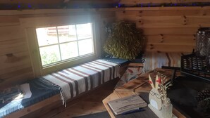 L’intérieur chaleureux d’un chalet avec un banc, une table sur laquelle se trouve un carnet, une plante décorative et une fenêtre laissant entrer la lumière naturelle.