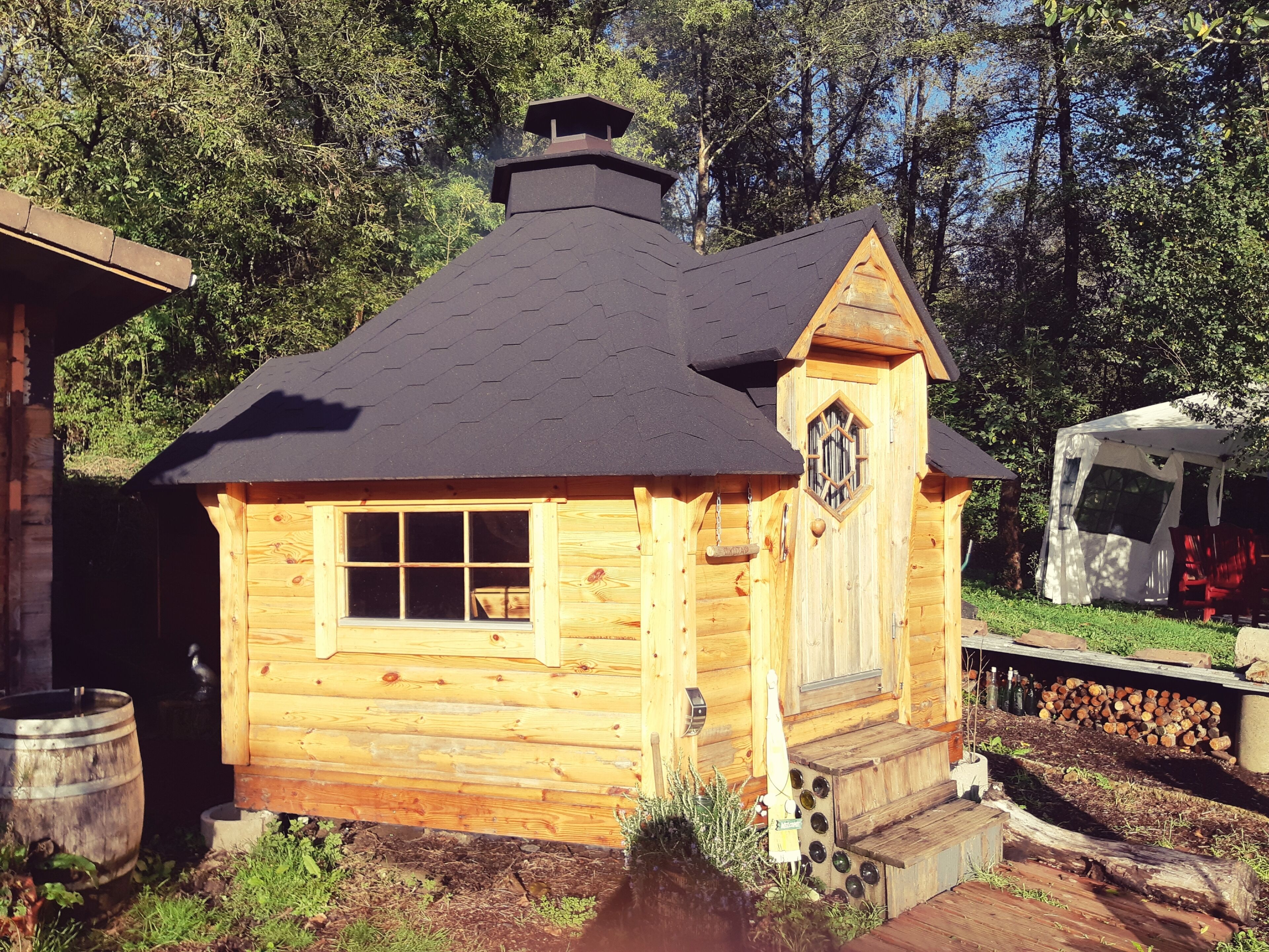 A wooden cabin with a black roof, a small porch, and a chimney.