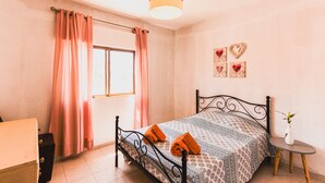 A bedroom with a bed, curtains, a bedside table with a vase, and heart-shaped decorations on the wall. - Charming 2-Bed Apartment in Armacao de Pera (Armacao de Pera)