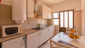 A kitchen with white cabinets, a microwave, a sink, and a window with blinds. - Charming 2-Bed Apartment in Armacao de Pera (Armacao de Pera)