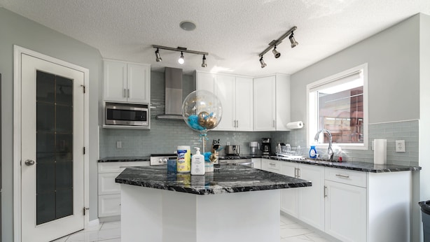 A modern kitchen with white cabinets, a granite countertop, and a large island. - G@Home Quiet 5BR4BA Retreat, Gateway to Banff & COP & Hwy 1 (Calgary)