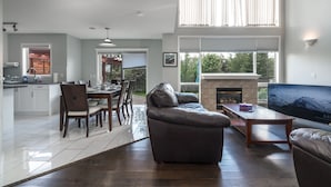 A modern living room with a leather sofa, dining area, kitchen, and a fireplace. - G@Home Quiet 5BR4BA Retreat, Gateway to Banff & COP & Hwy 1 (Calgary)