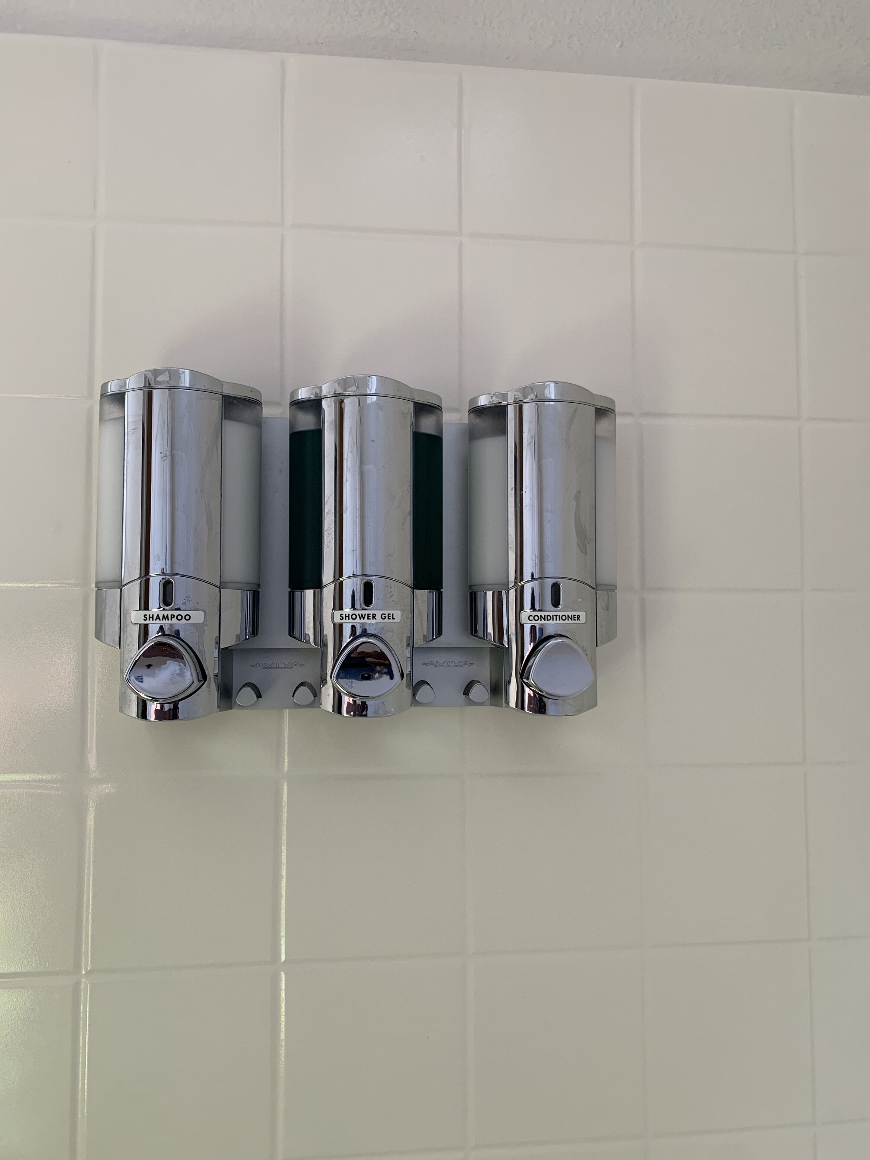 A wall-mounted dispenser with three compartments labeled shampoo, shower gel, and conditioner.