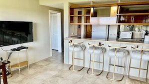 A modern kitchen with a bar area, a television, and a door leading to another room. - Best View in Hilo - Pool, WIFI, 2 BD Condo (Hilo)