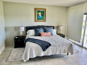 Une chambre à coucher avec un grand lit, deux tables de chevet, une commode, une fenêtre avec des stores et un tableau au mur.