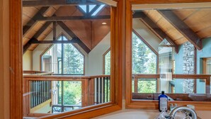 A bathroom with a large window, wooden beams, and a stone wall.