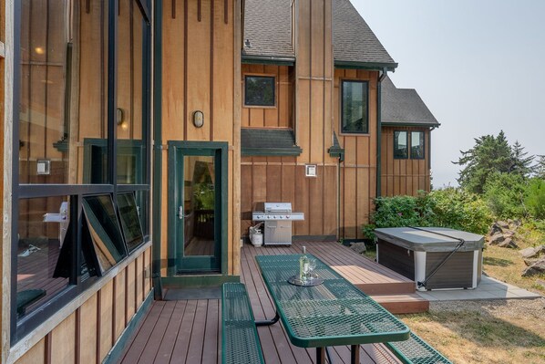 A wooden building with a patio area featuring a grill, a table with wine glasses, and a hot tub.