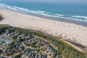 An aerial view of a coastal area with a sandy beach and a row of wooden cabins with steep roofs.