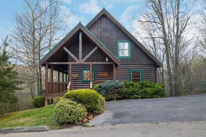 Une cabane en rondins dotée d’un porche, entourée de verdure et d’arbres.