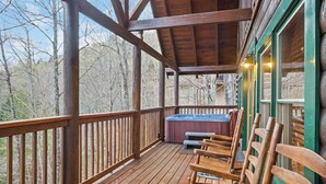 A wooden deck with a hot tub and chairs, surrounded by trees.