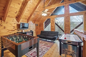Un intérieur chaleureux d’une cabane en bois, avec un baby-foot, un canapé et une table de hockey sur glace.