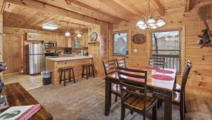A wooden cabin interior with a kitchen, dining area, and a large window.