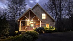 A log cabin with a porch, a visible sign, and a well-maintained lawn.