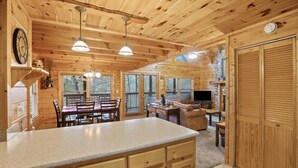 A wooden cabin interior with a kitchen, dining area, and living room.