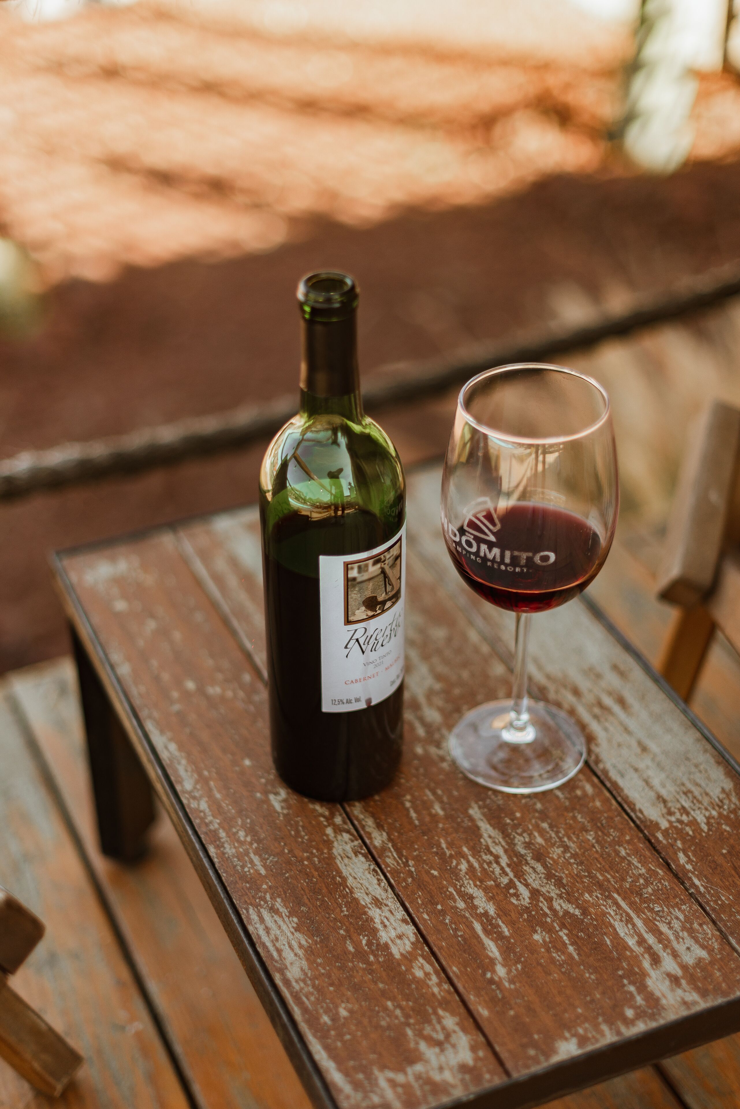 Una botella de vino tinto y una copa sobre una mesa de madera.