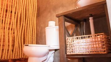 Ein modernes Badezimmer mit Holzboden, Toilette in Weiß, einem gewebten Korb und einem Spiegel auf einer Holzablage.