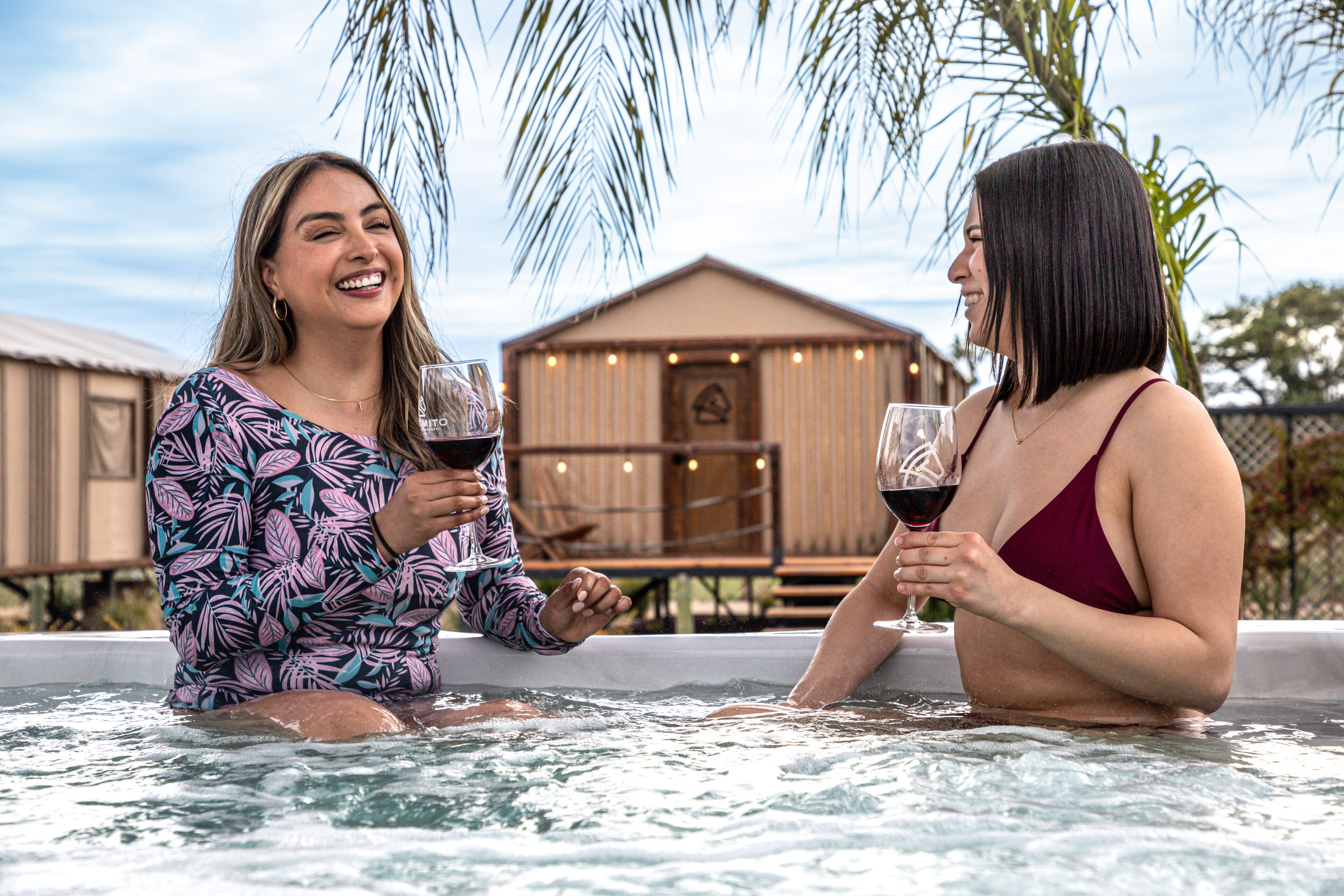 Two people in a hot tub with a wooden building in the background.