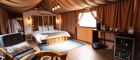A spacious bedroom with a large bed, a wooden coffee table, a chair, and a minibar.