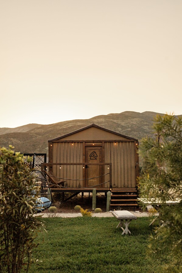 A rustic wooden cabin with a front door, a small porch, and a staircase leading up to it. - Indomito Resort & Hotel Boutique (Valle de Guadalupe)