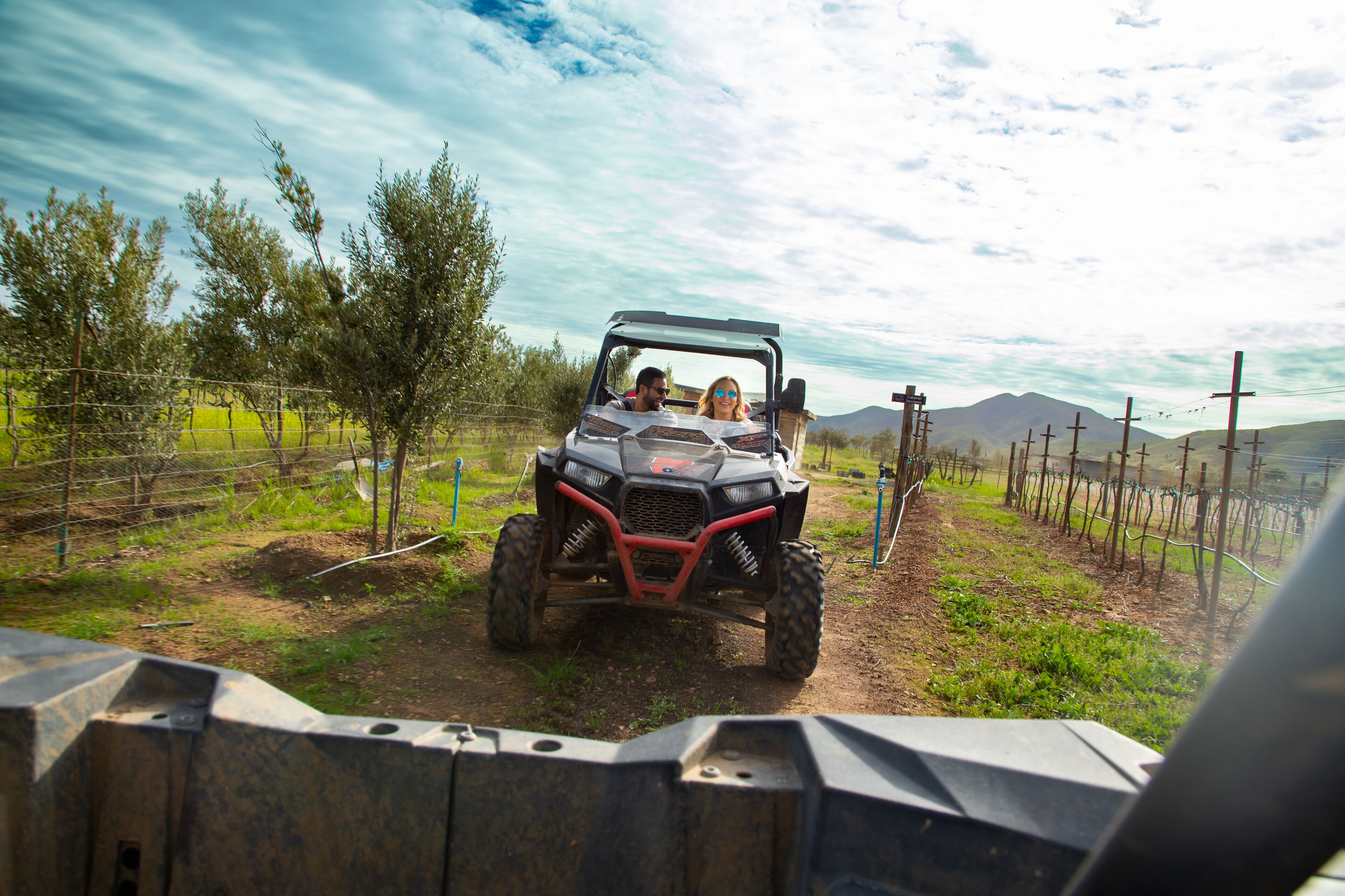 A vehicle on a dirt path with a fence and trees in the background.