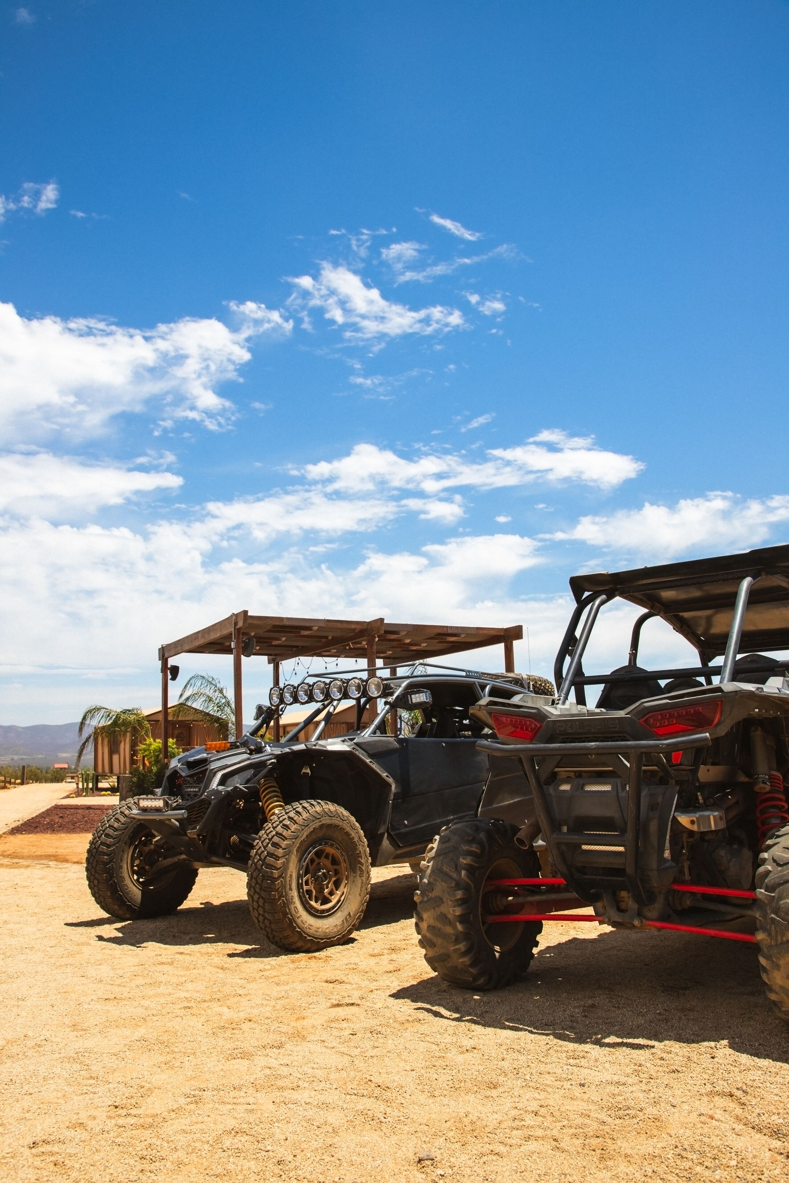 Two off-road vehicles parked in a sandy area with a clear sky.