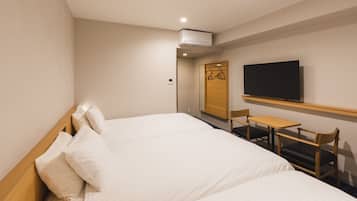 A hotel room with a large bed, a small table, two chairs, a TV, and an air conditioning unit.