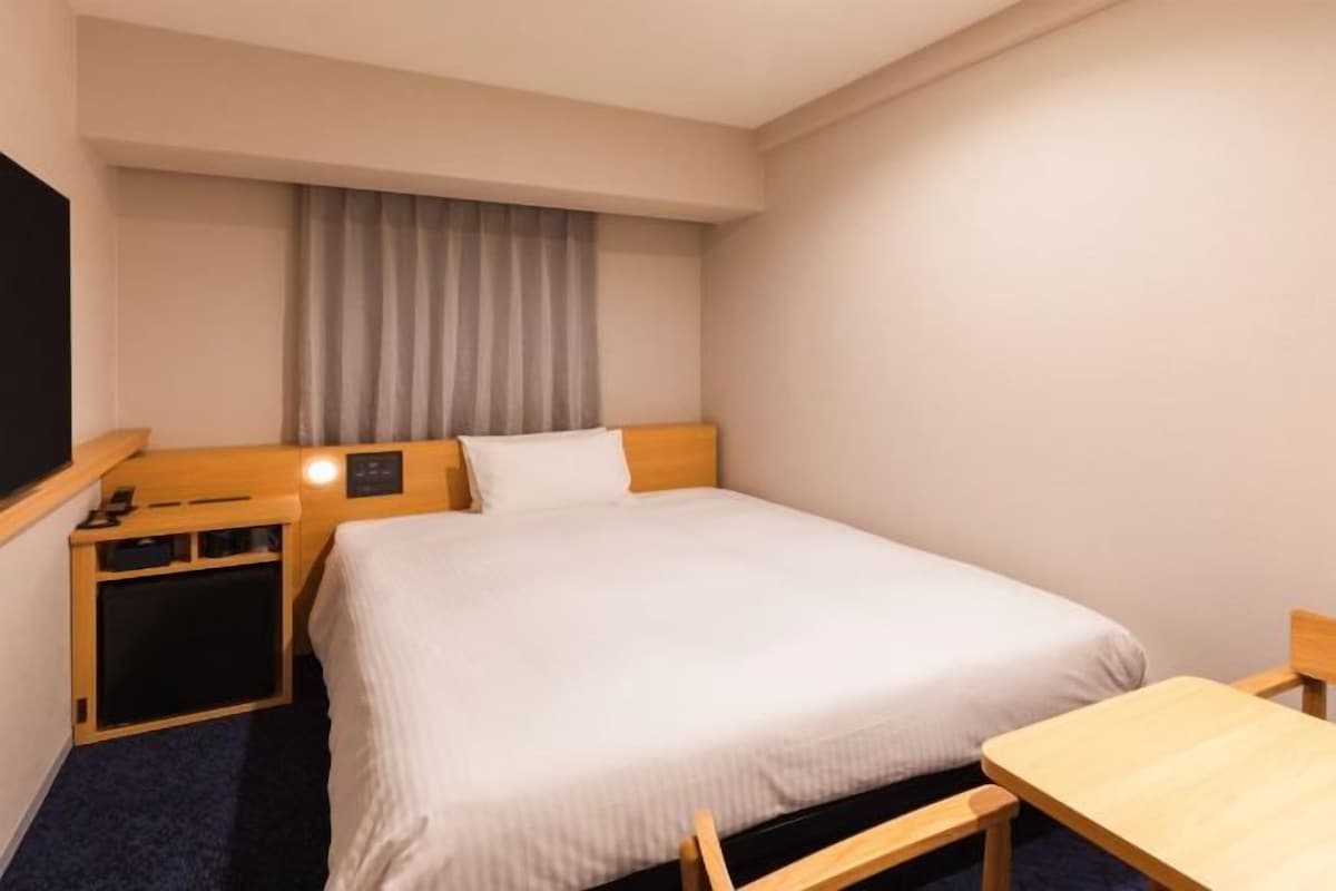 A hotel room with a single bed, a bedside table, a small desk, a chair, and a television.