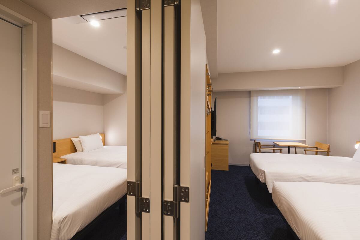 Habitación de hotel con dos camas, un escritorio, una silla y un ventanal.