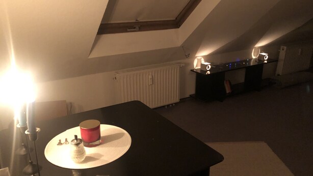 Ein schwach beleuchteter Raum mit einem Tisch, einem Heizkörper und einem Schreibtisch mit einer Lampe.