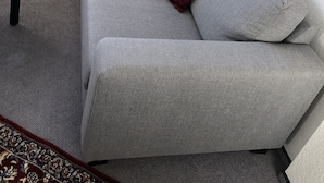 Ein graues Sofa mit zwei Kissen, ein kleiner Tisch und eine Heizung in einem Eckzimmer.
