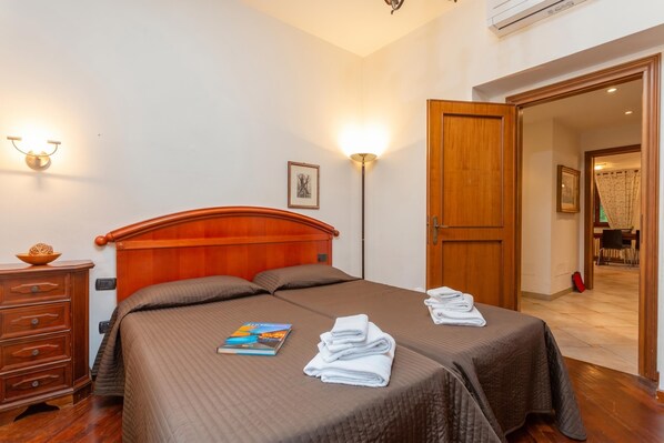 Une chambre d’hôtel avec un lit en bois, deux tables de chevet, une lampe et une porte donnant sur un coin repas.
