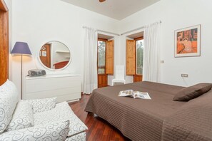Une chambre à coucher avec un lit, une table de chevet, une lampe, un miroir et une fenêtre avec des rideaux.