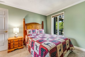 Un dormitorio con cama de madera, una mesita de noche con lámpara y vista a zonas verdes por la ventana.