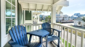 Een balkon met twee blauwe Adirondack-stoelen en een kleine tafel, met uitzicht op een woonwijk met huizen en een heldere lucht.