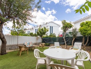 A backyard with a white table and chairs, surrounded by a white fence and greenery.