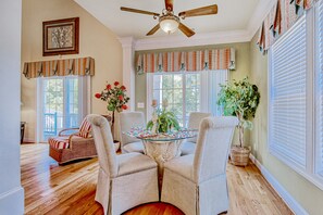 A dining area with a round table, four chairs, a ceiling fan, and large windows with curtains. - Bright, expansive home near the beach with enclosed yard & large deck (North Myrtle Beach)