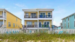 A beachfront property with a two-story building featuring balconies, a white fence, and a grassy foreground. - Oceanfront Escape: 5BR Beach House w/ Pool for 12 (Gulf Shores)