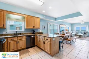 A spacious kitchen with wooden cabinets, a dishwasher, and a dining area with a table and chairs. - Gulf Shores Paradise: Beachfront 5BR + Pool + Views (Gulf Shores)