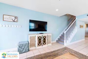 A living room with a flat-screen TV, a staircase, and a wall-mounted artwork. - Gulf Shores Paradise: Beachfront 5BR + Pool + Views (Gulf Shores)
