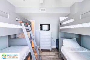 Une chambre avec un lit superposé, une échelle, un téléviseur posé sur un meuble et le logo de Destination Vacation.