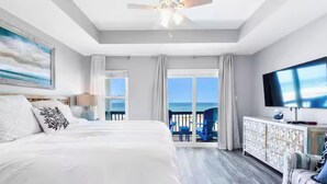 A hotel room with a large bed, a ceiling fan, a TV, and a balcony with a view of the ocean. - Oceanfront Escape: 5BR Beach House w/ Pool for 12 (Gulf Shores)