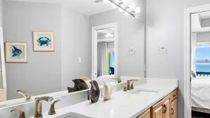 A bathroom with a large mirror, two framed pictures on the wall, and a sink with a modern faucet. - Oceanfront Escape: 5BR Beach House w/ Pool for 12 (Gulf Shores)