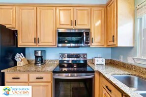 A kitchen with wooden cabinets, a stainless steel microwave, a coffee maker, a toaster, and a sink.