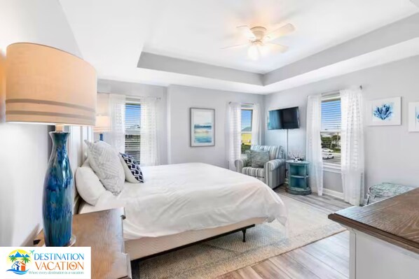 A bedroom with a bed, a bedside table, a lamp, a ceiling fan, and a window with curtains.