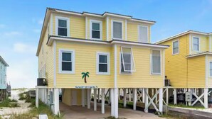 A yellow building with a white porch and a palm tree sign. - Oceanfront Escape: 5BR Beach House w/ Pool for 12 (Gulf Shores)
