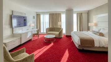 A hotel room with a bed, a desk, a chair, a television, and a red carpet.