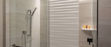 Un baño moderno con ducha de mampara de vidrio, barra de apoyo y estante con artículos de aseo.