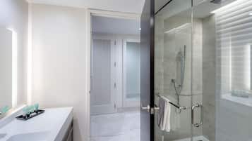 A modern bathroom with a glass-enclosed shower, a vanity with toiletries, and a door leading to another room.